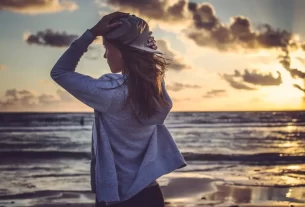 Mulher olhando para o horizonte ao pôr do sol, com expressão de liberdade, leveza e esperança, representando autoconhecimento e conexão com a vida. cura emocional e trasformação