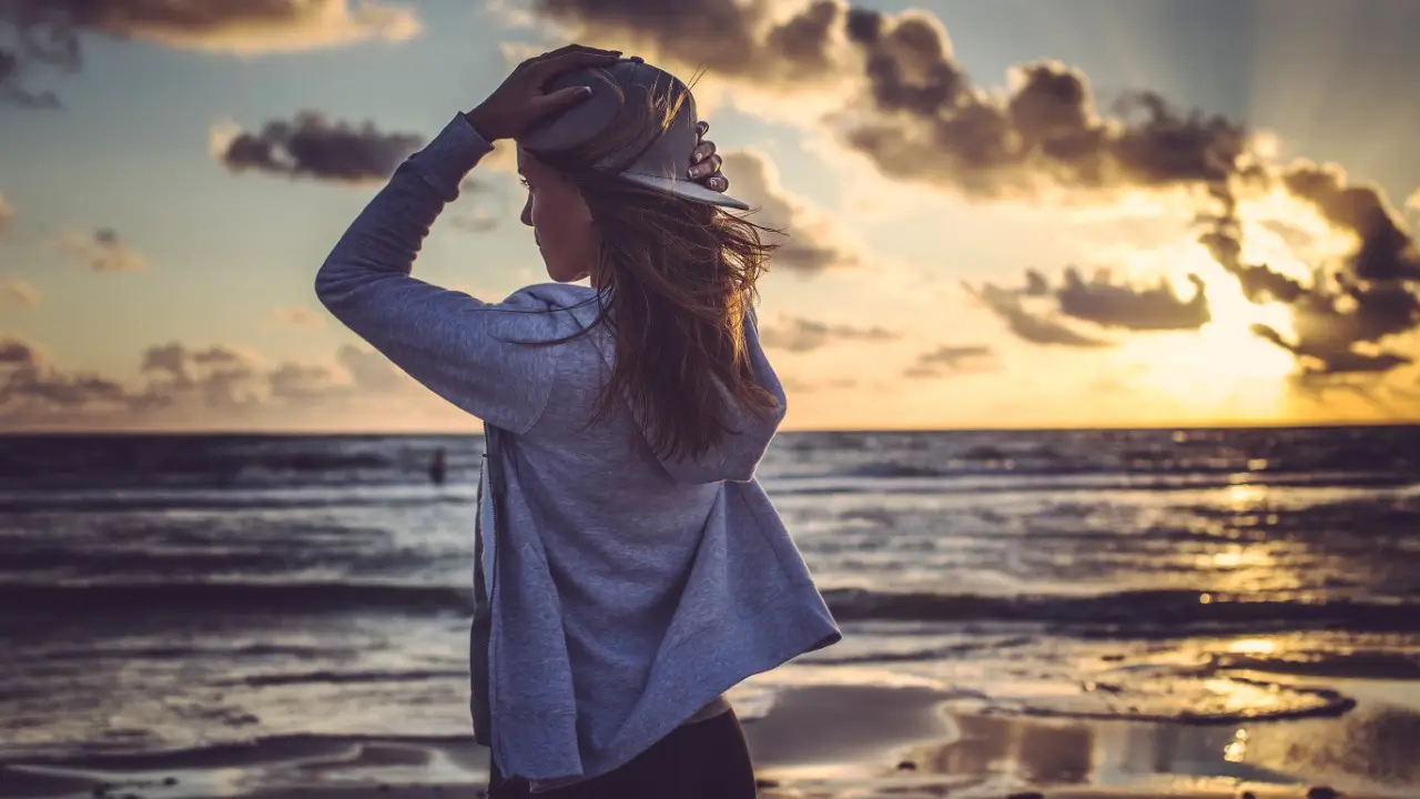 Mulher olhando para o horizonte ao pôr do sol, com expressão de liberdade, leveza e esperança, representando autoconhecimento e conexão com a vida. cura emocional e trasformação