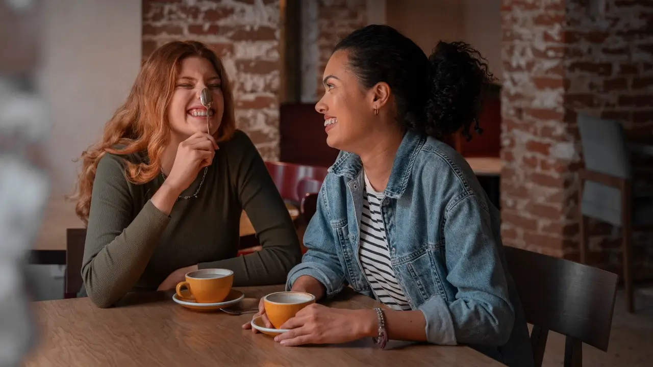 “Duas amigas conversando e rindo ao ar livre, com celulares desligados, representando conexões autênticas e relações verdadeiras na era digital