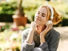 Mulher sorrindo de olhos fechados, ouvindo música com fones, sentindo a influência da música na vibração energética do seu corpo.