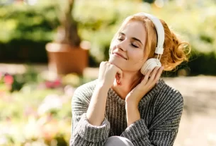 Mulher sorrindo de olhos fechados, ouvindo música com fones, sentindo a influência da música na vibração energética do seu corpo.