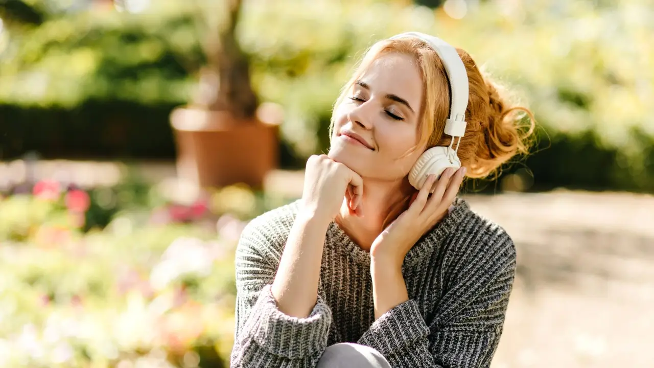 Mulher sorrindo de olhos fechados, ouvindo música com fones, sentindo a influência da música na vibração energética do seu corpo.