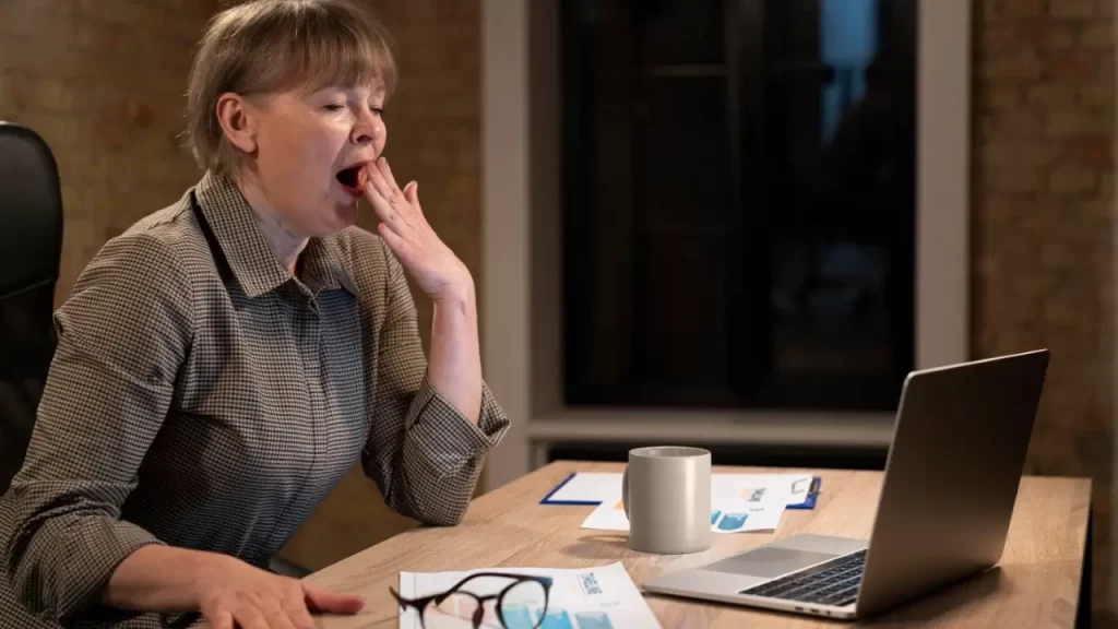 burnout e preguiçe indentifique, mulher bocejando na mesa de trabalho
