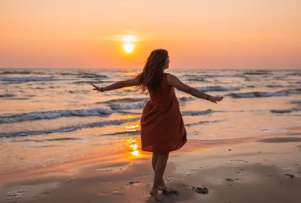 mulher de braços abertos em campo iluminado pelo nascer do sol, representando o renascimento da mulher na nova era
